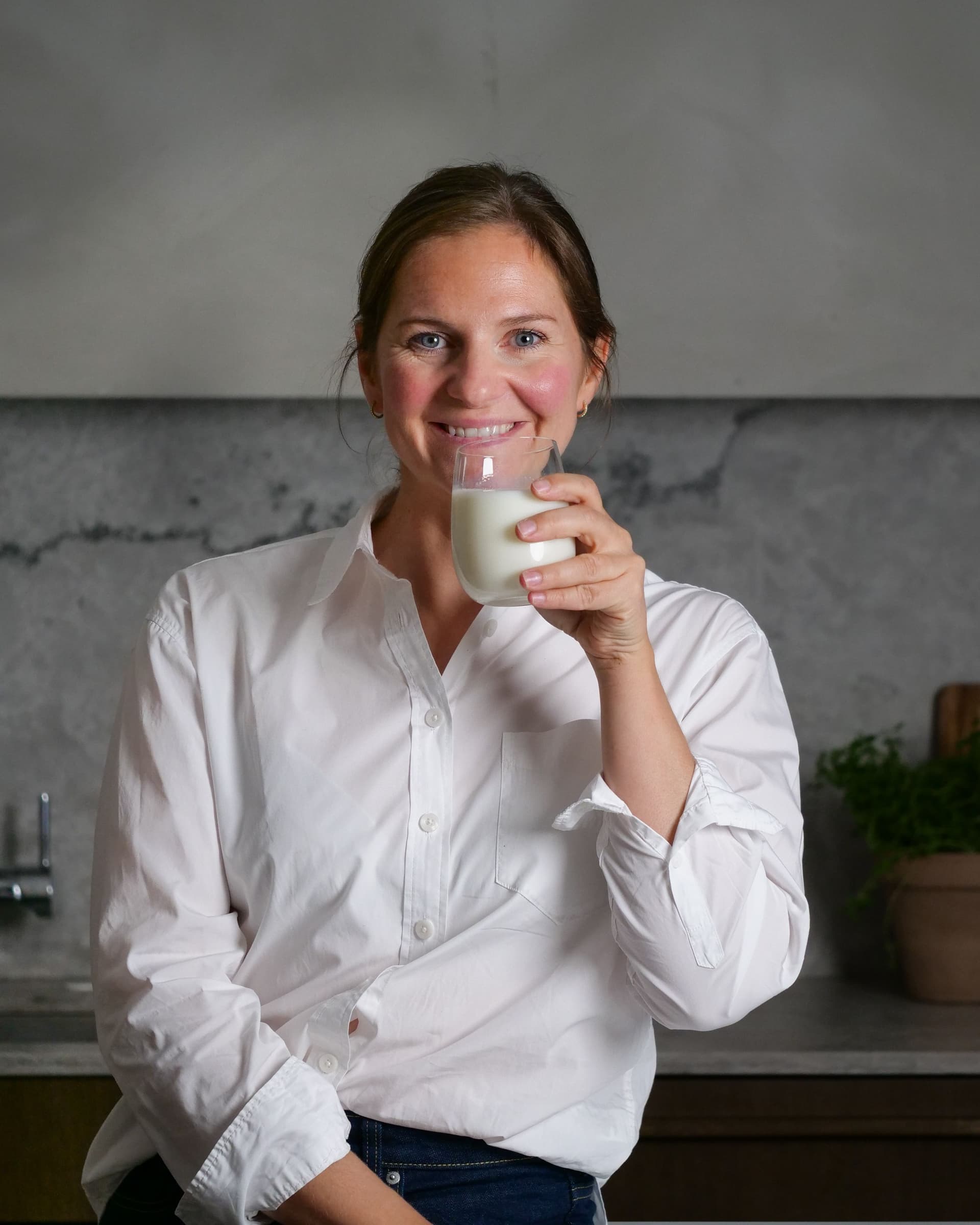 Kvinne med hvit skjorte smiler og holder et melkeglass